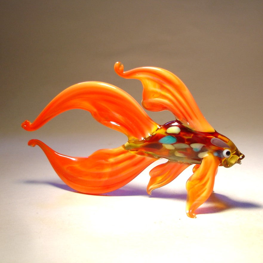 A side view of the orange Betta fish glass figurine, highlighting the flowing, fan-like fins and tail that extend gracefully behind the fish.