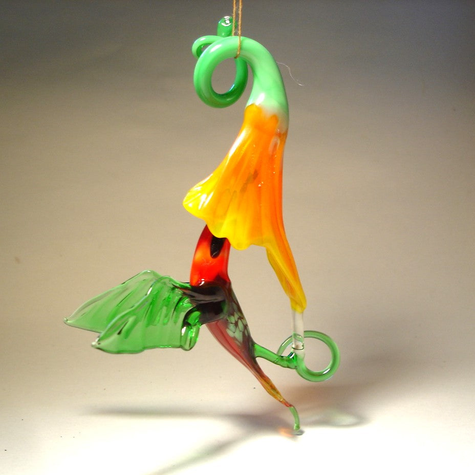 Suspended glass ornament featuring a red head hummingbird in flight with a yellow trumpet flower.