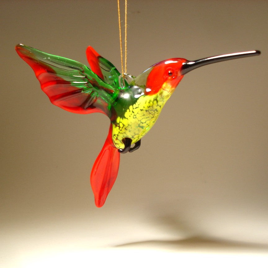 A vibrant red, green and yellow glass hummingbird ornament with a long pointed beak.