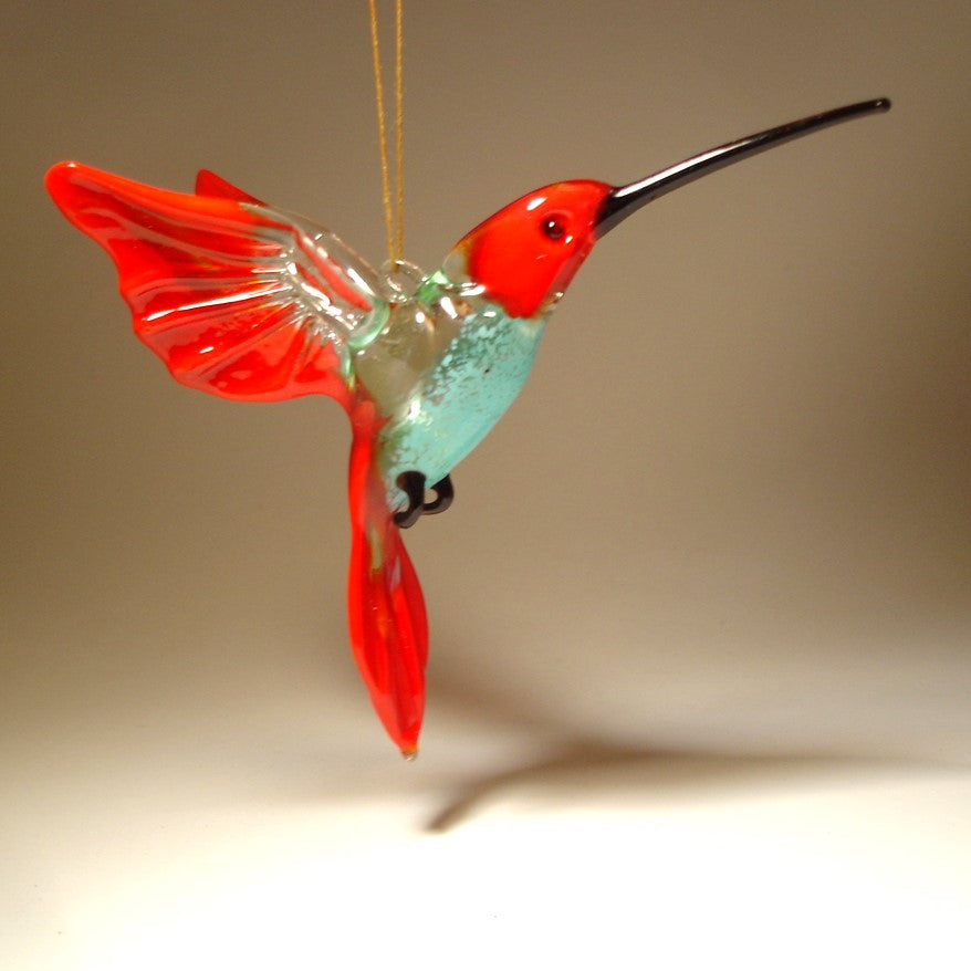 A side view of the red and blue glass hummingbird ornament, emphasizing the elegant curve of its body and wings.