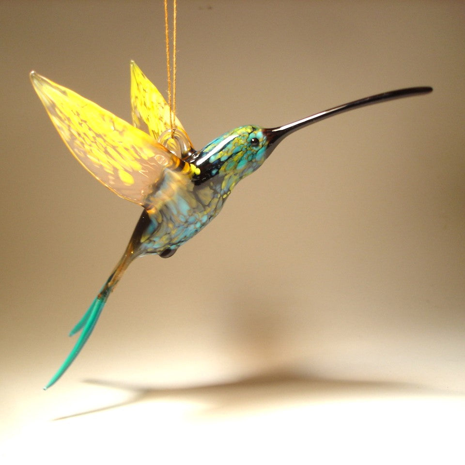 Side view of a glass, blue and Yellow swallowtail hummingbird ornament suspended from a thread.