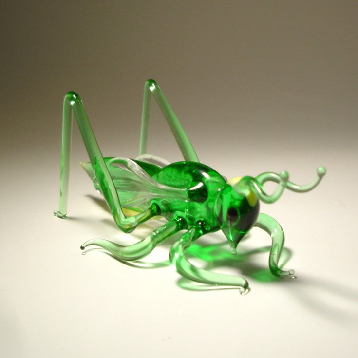 Green glass grasshopper on a beige background