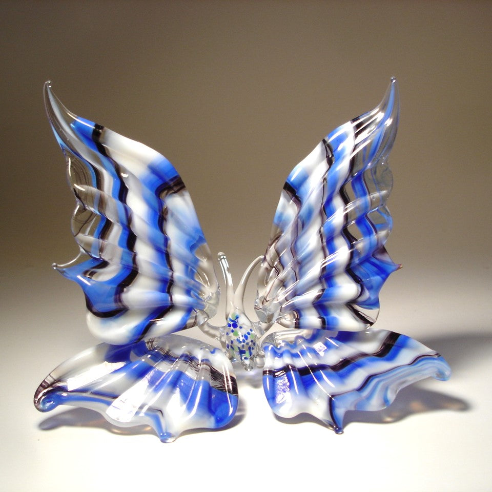 A front view of a white, blue and black striped glass butterfly figurine with intricately designed wings.