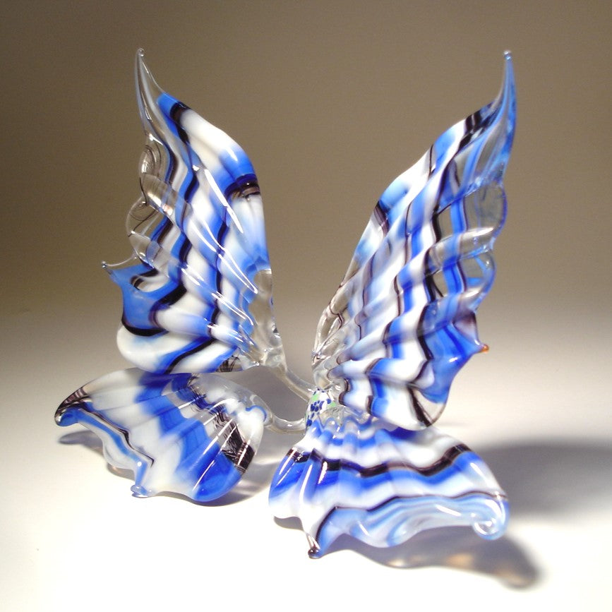 A side view of a white and blue striped glass butterfly figurine, highlighting the elegant curves of its wings and the detailed blue stripes.