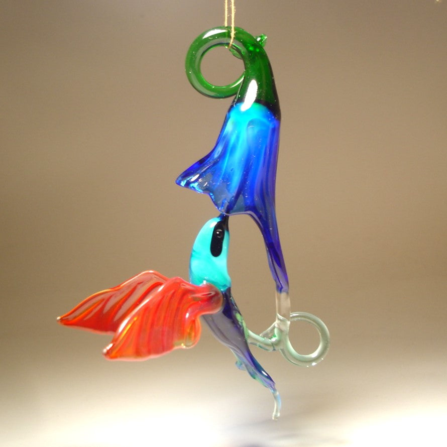 Glass ornament featuring a hummingbird drinking nectar from a blue trumpet flower.