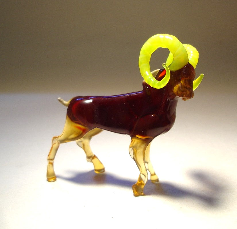 Close-up of a handmade glass mountain goat figurine featuring striking yellow curled horns.