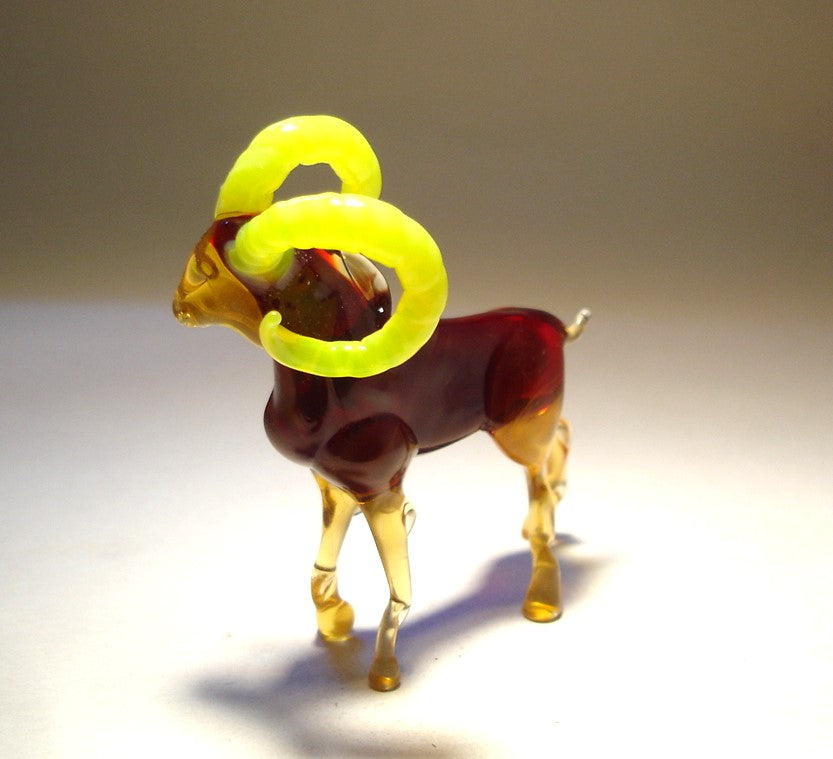 Side view of the glass mountain goat, showcasing its powerful stance and the vibrant contrast between its clear body and the bright yellow horns.