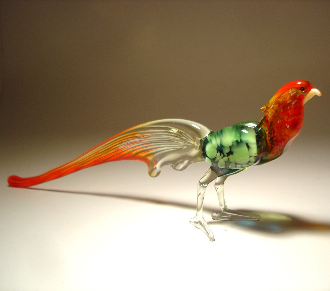 Side angle of the glass pheasant figurine, capturing the elegant curve of its long red and clear tail feathers.