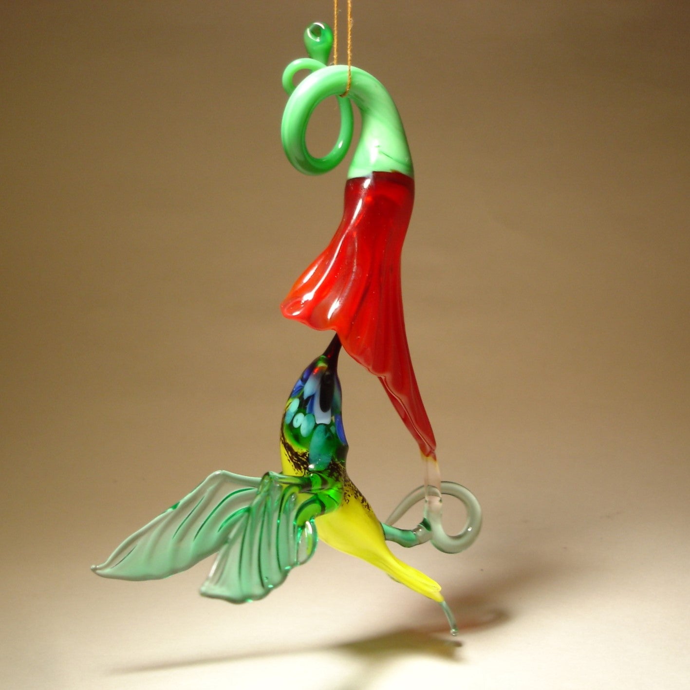 Glass hanging hummingbird ornament on a red trumpet flower.