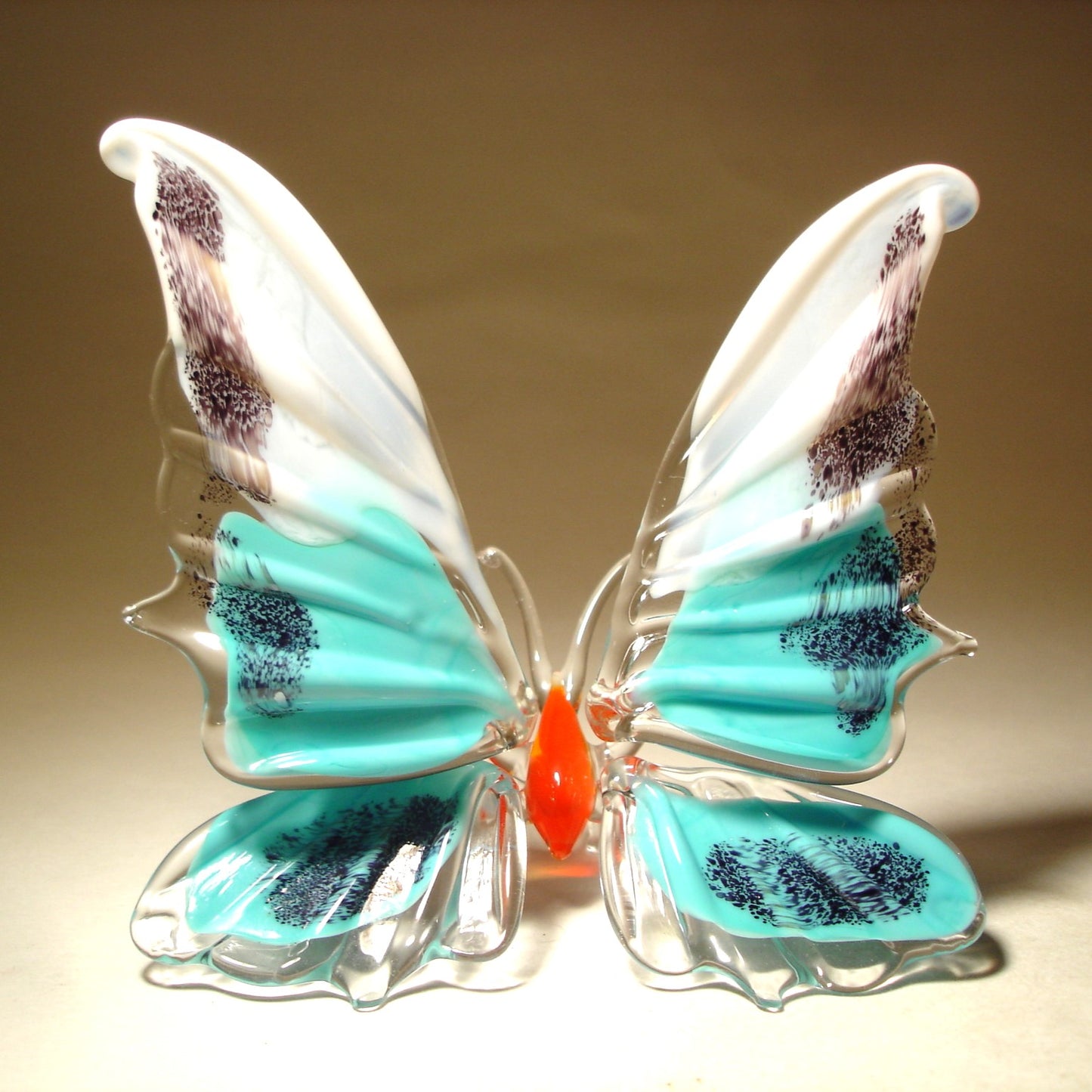A white and aqua blue glass butterfly figurine with red body, sitting.