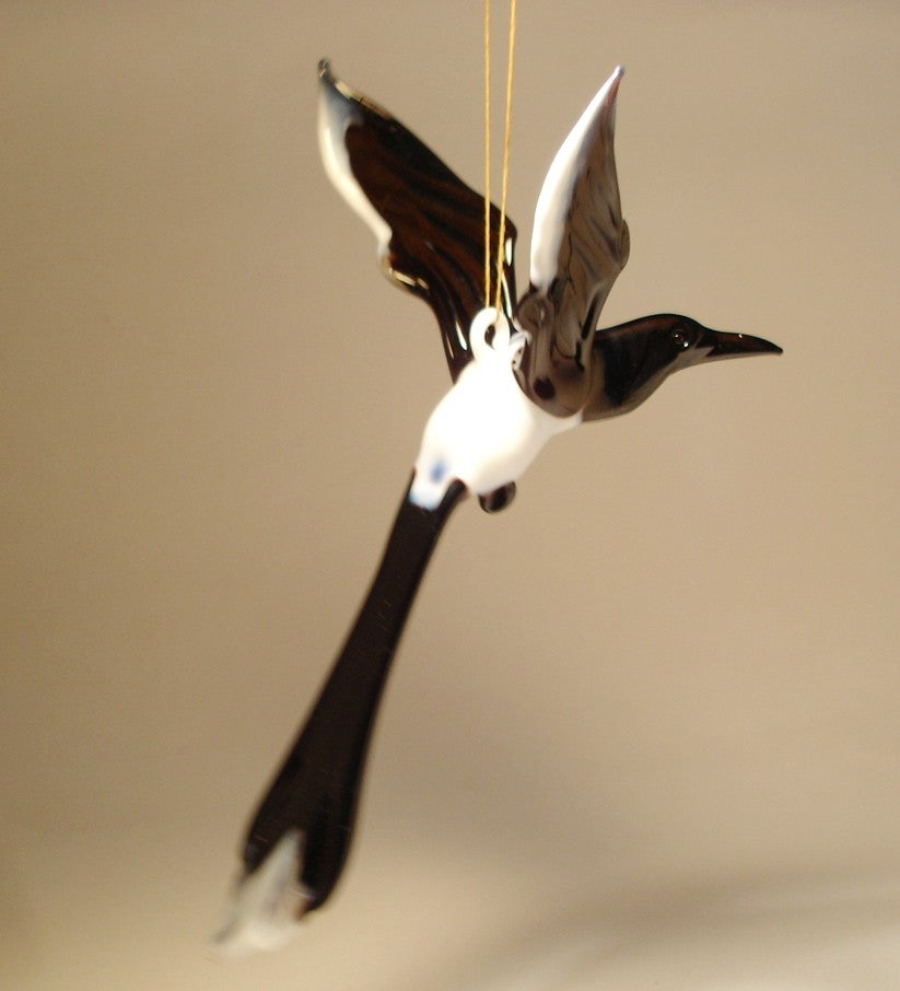 A glass Hanging Bird Magpie figurine ornament, suspended from a thread, showcasing its distinctive black and white feathers