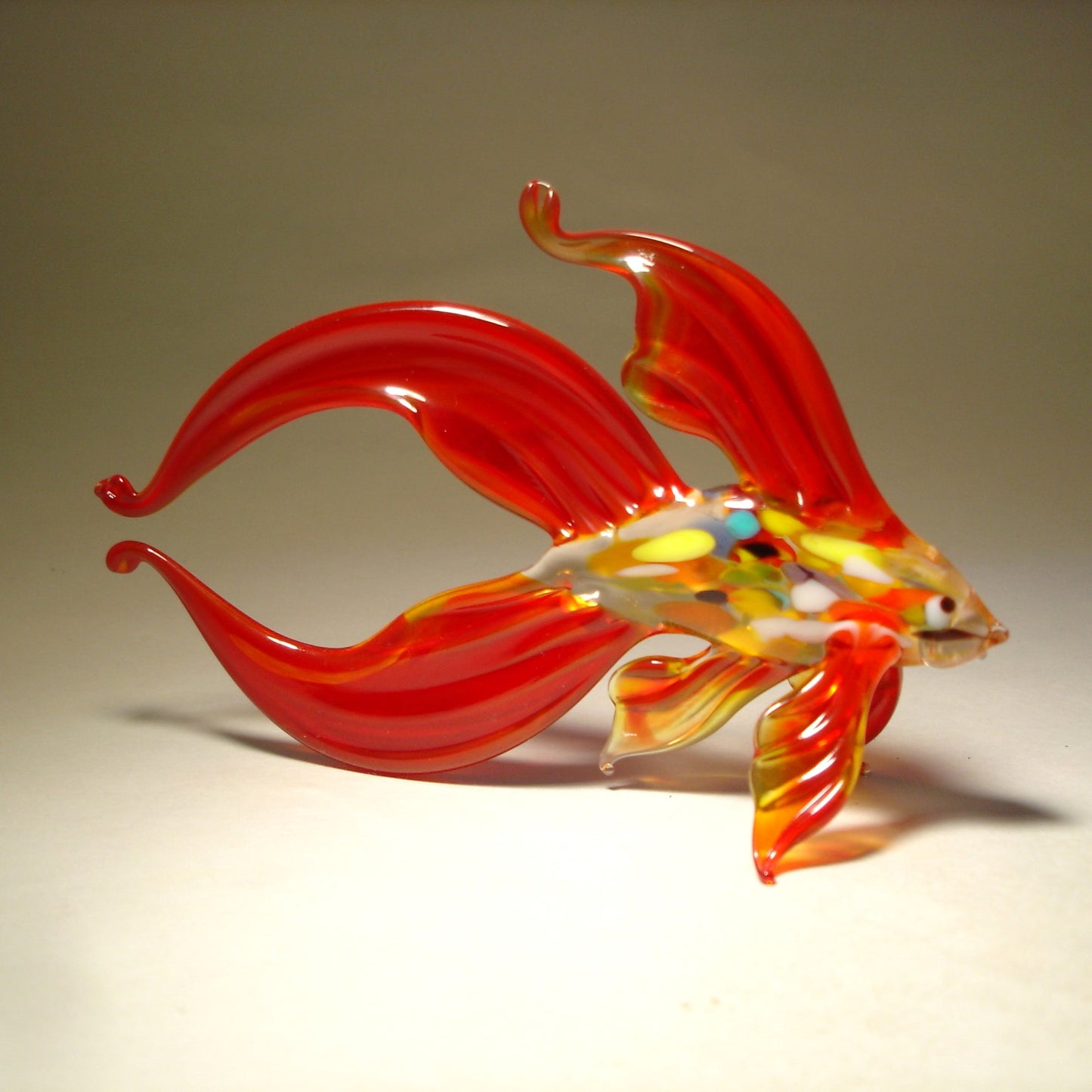 A side view of a dark red glass betta fish figurine, highlighting the graceful curves of its body and the delicate texture of its fins.