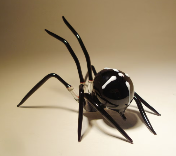 Top view of a handcrafted black glass spider figurine highlighting the white cross on its back
