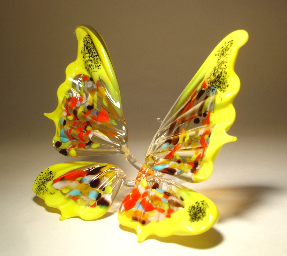 The other side view of the glass butterfly figurine, with its wings trimmed in yellow and multicolored specs filling the rest of the wings.