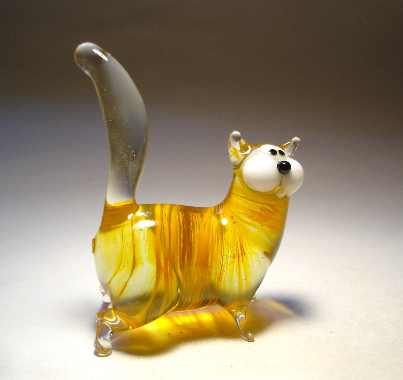 A side view of the glass chubby cat figurine with white face, highlighting its plump body and upright clear glass tail.