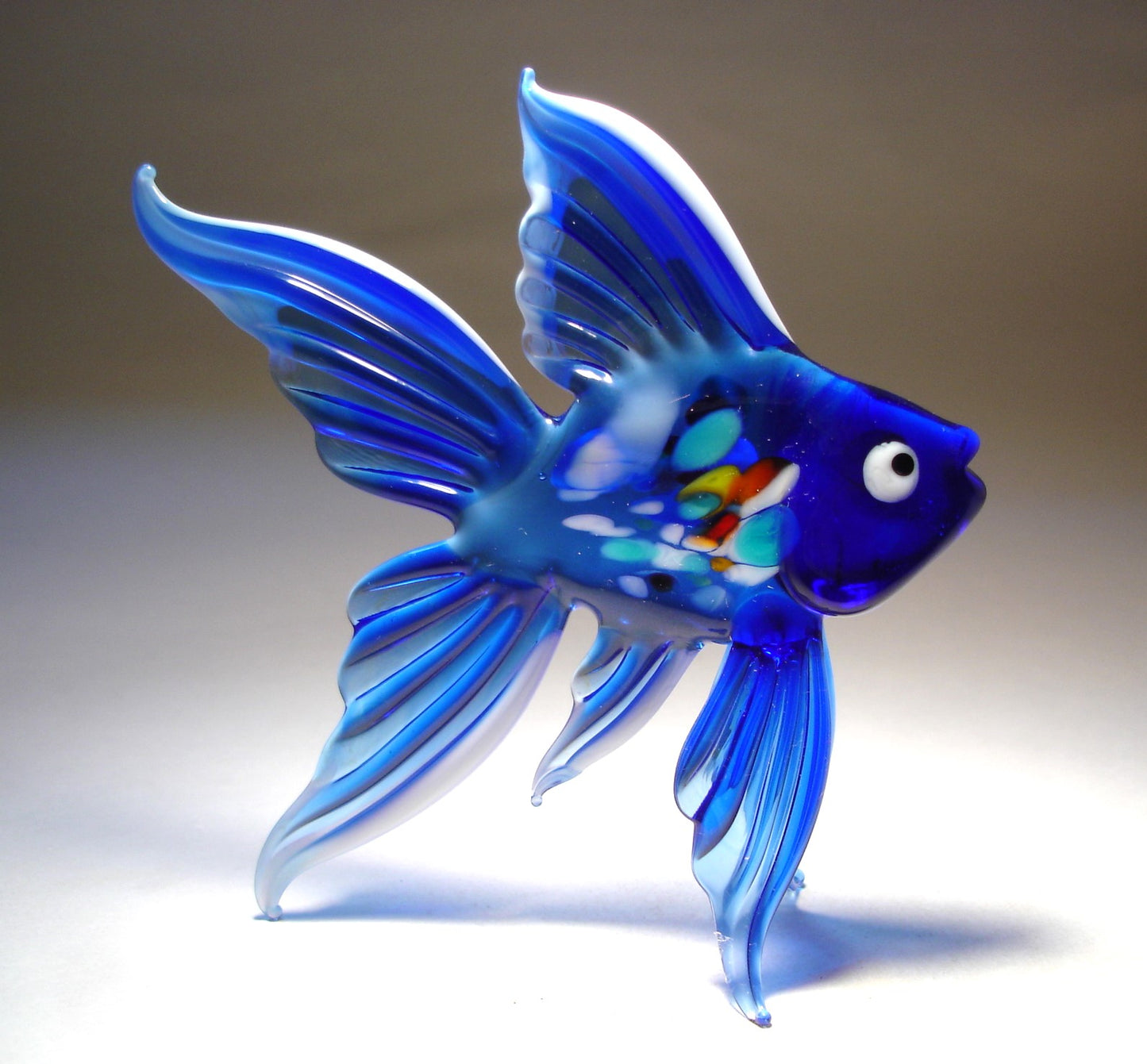Opposite side view of a handmade blue glass and white fish figurine, showcasing its vibrant blue body