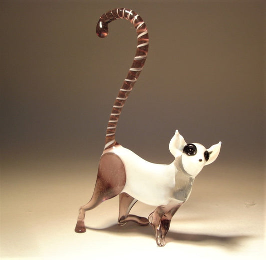 Side view of a white and lilac glass monkey lemur figurine, illustrating its dynamic pose with a curled striped tail.