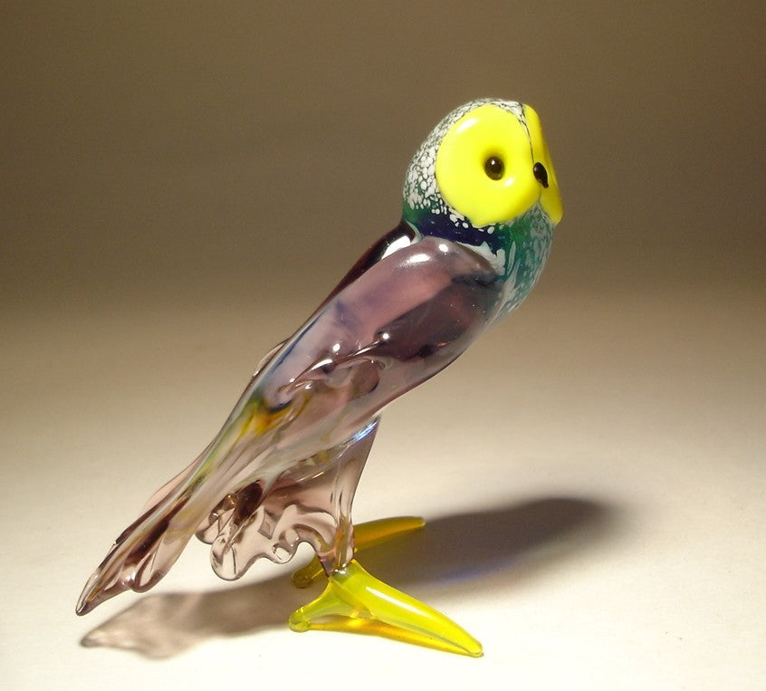 Side view of the lilac and green glass owl, showcasing its charming expression and the vibrant contrast between the lilac body, green wings, and yellow face.