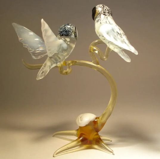Side angle of a glass figurine showcasing two polar owls on a branch, one has its wings open. The owls are sitting together on an elegantly curved branch.