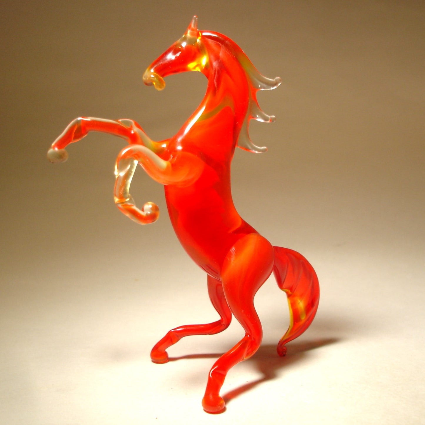 A side view of the red glass horse figurine, highlighting the elegant curves of its rearing body and the flowing tail.