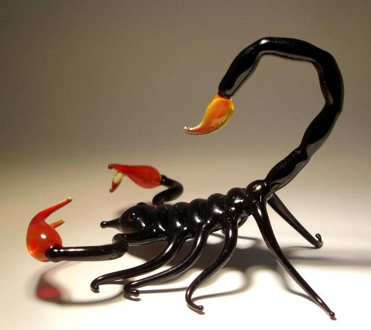 A front view of a black glass scorpion figurine, showcasing its glossy black body, detailed red claws, and a red stinger.