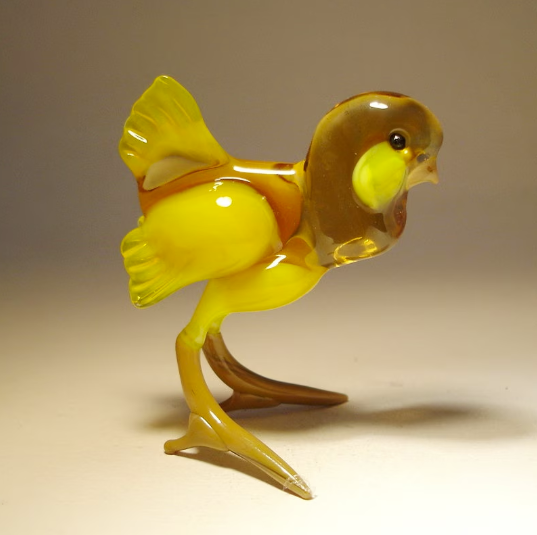Close-up of a cheerful yellow glass chicken figurine, showcasing its intricate detailing of the beak, cheeks and wings.