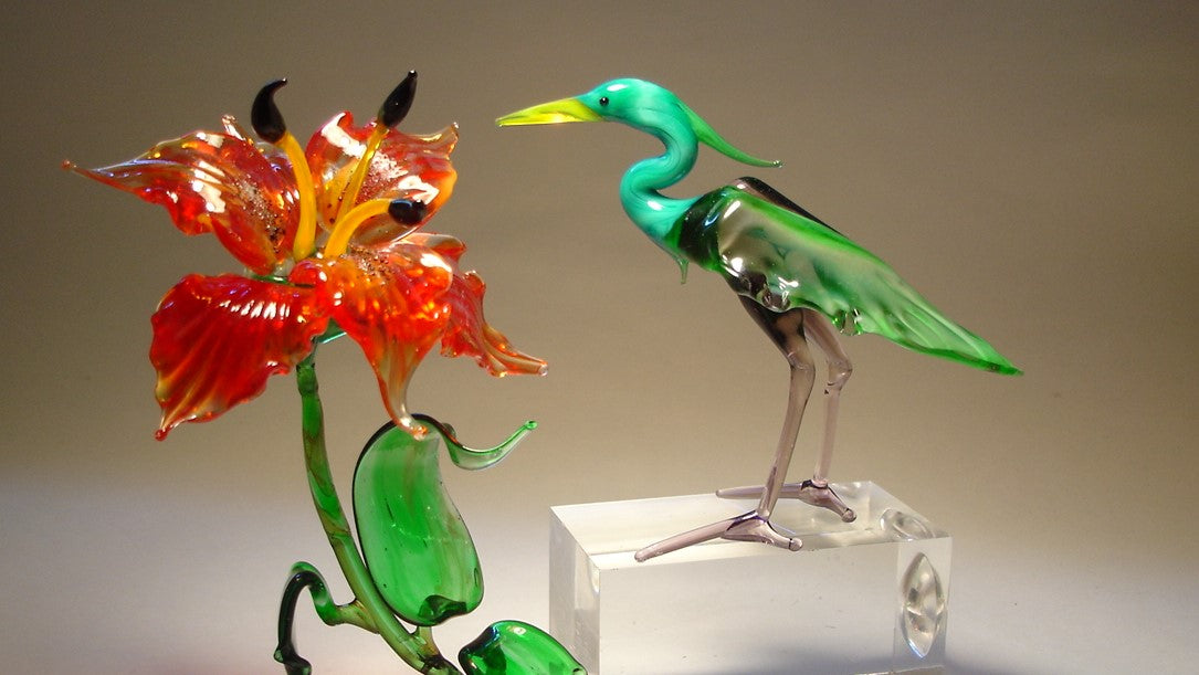 A glass lily flower and a glass heron next to it.