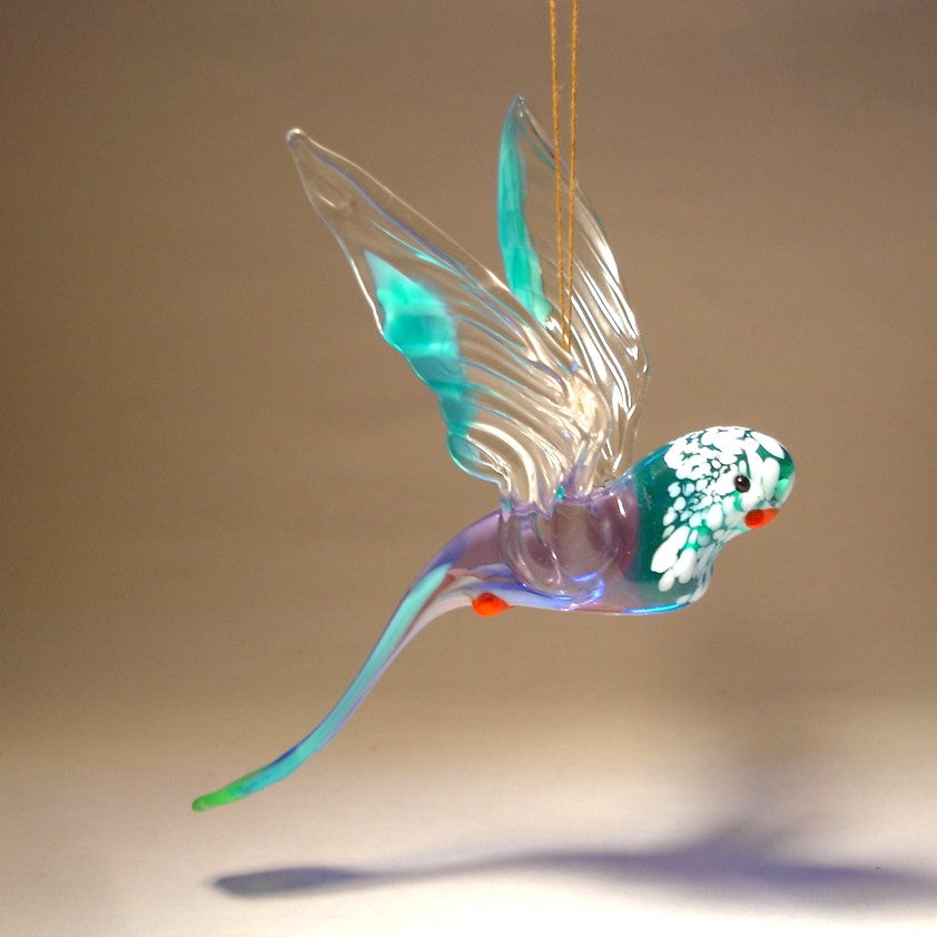 The glass parakeet ornament is depicted in striking blue and white hues with red beak and feet.