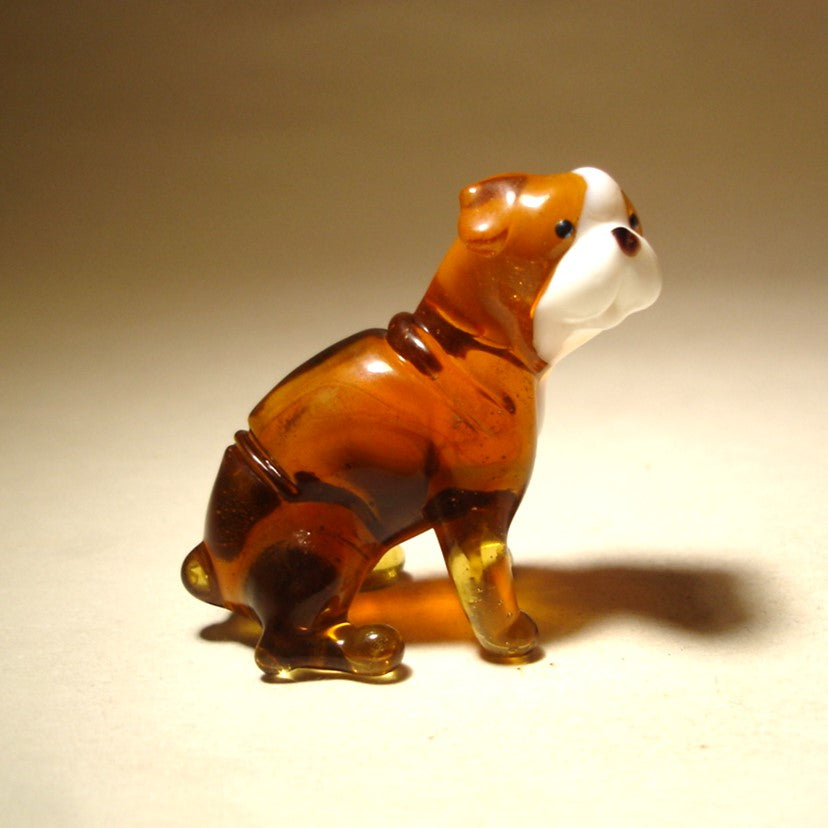 A detailed glass figurine of a sitting English Bulldog with a glossy finish in shades of brown and white.