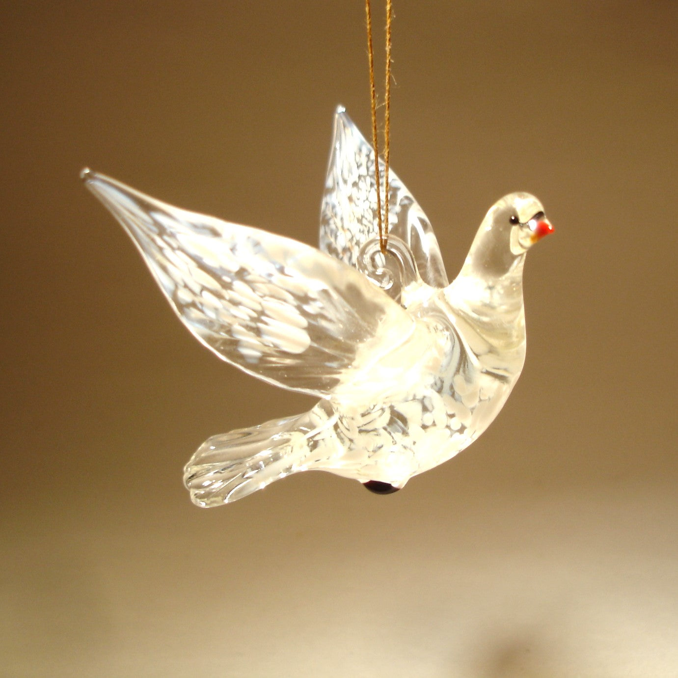 A delicate glass dove ornament gracefully suspended in mid-flight, showcasing its  intricate feather details in white and clear glass.