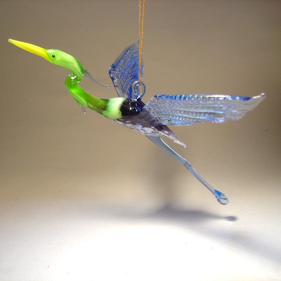 Side view of the Glass Heron in Flight Hanging Figurine, highlighting the bird's graceful posture and elongated neck mid-flight.