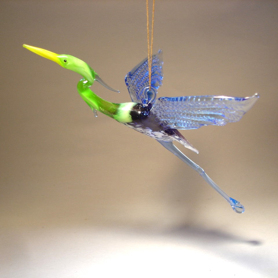 Angled view of the Glass Heron in Flight Hanging Figurine Ornament, showcasing its blue and green body and long legs.