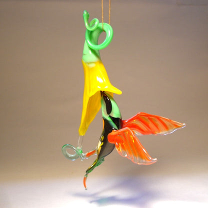 Suspended glass ornament featuring a green head hummingbird in flight with a yellow trumpet flower.