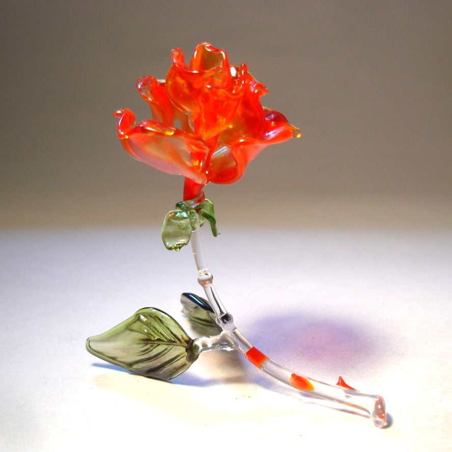 A side view of a red glass rose figurine, showcasing its intricate petals and a stem with red thorns.