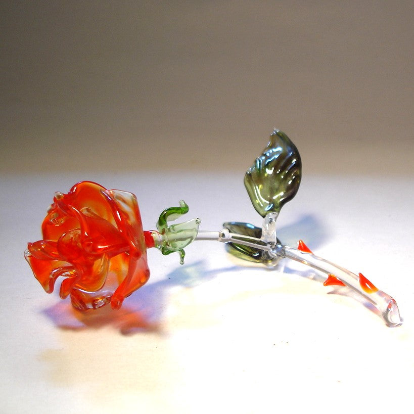 A red rose glass figurine is laying on a side showcasing the details of its beautiful red petals.