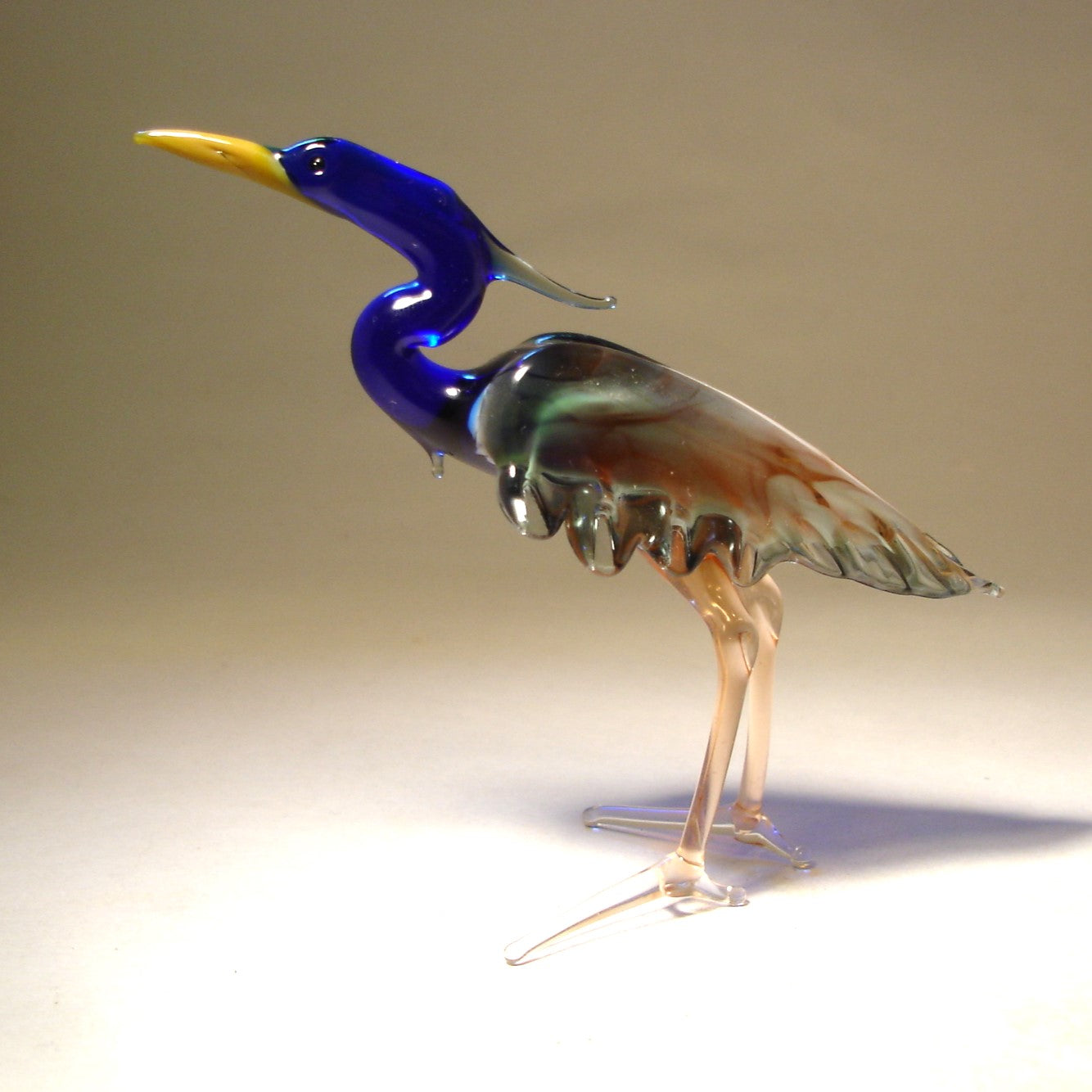 Side view of the glass heron figurine, highlighting the detailed green and brown wings and slender legs.