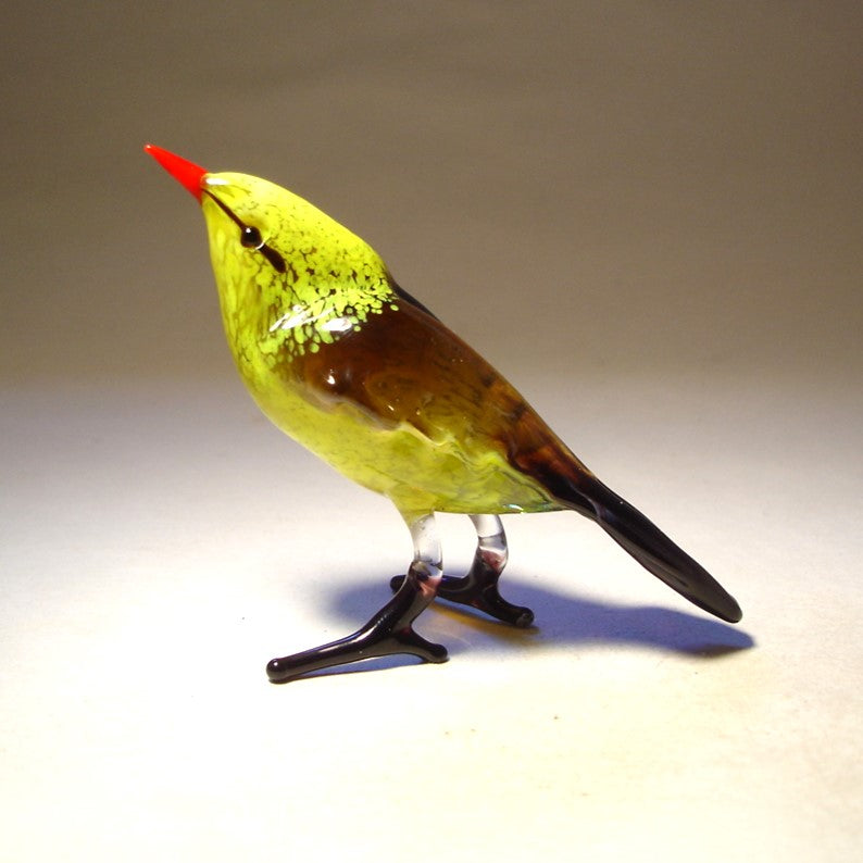 A front view of a yellow glass bird figurine featuring a bright red beak, showcasing its smooth body, detailed eyes, and a cheerful expression.