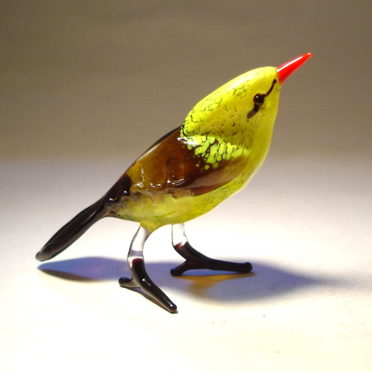 A side view of the yellow glass bird figurine, highlighting its elegant silhouette, the contrast between the vivid yellow body and the striking red beak.