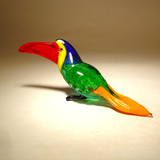  front view of a glass toucan figurine featuring a vibrant red beak, showcasing its green and orange body with a blue head.