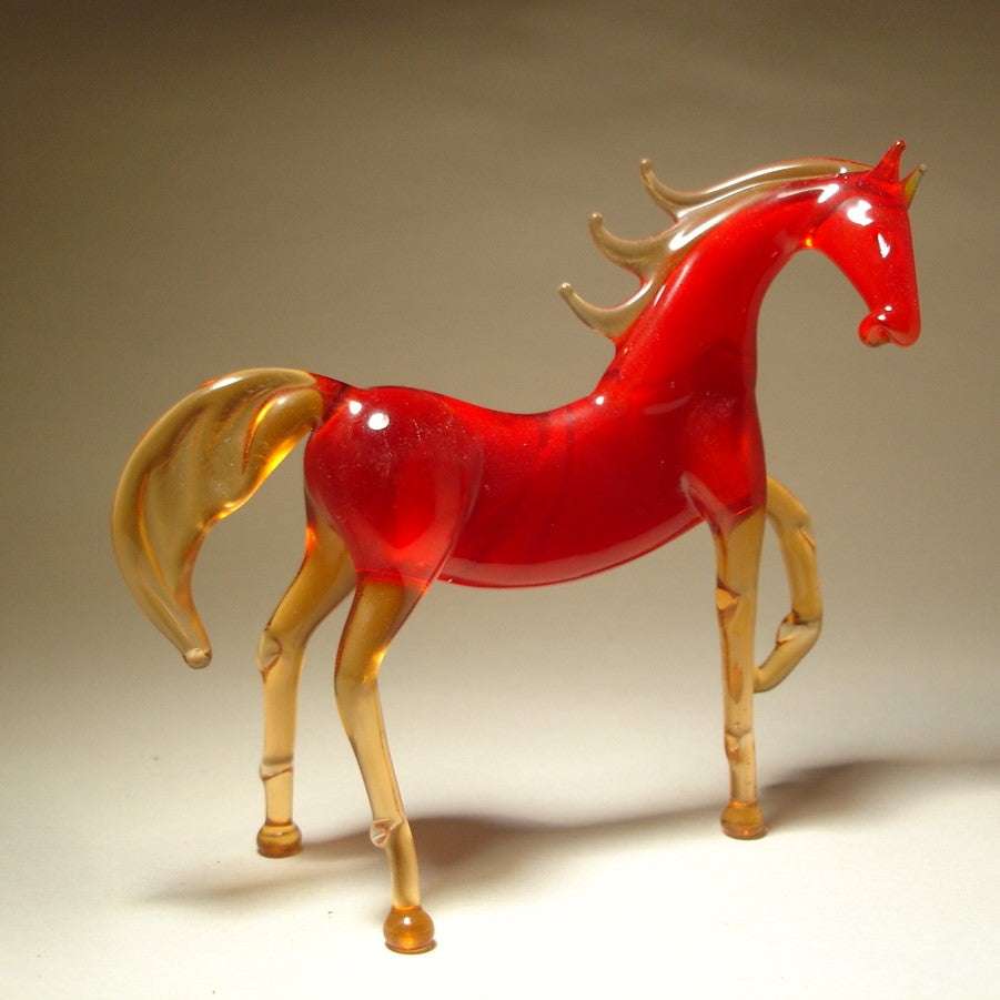 A side view of a handmade red glass horse figurine, highlighting its raised left foot and flowing tail.