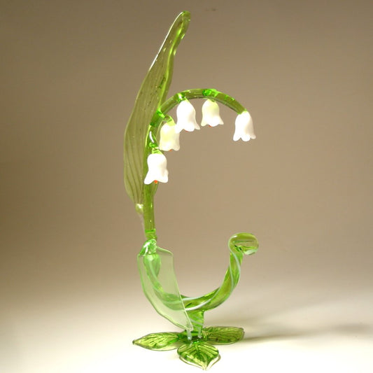 A delicate glass Lily of the Valley flower figurine, showcasing its slender stem, green leaves  and white bell-shaped flowers.