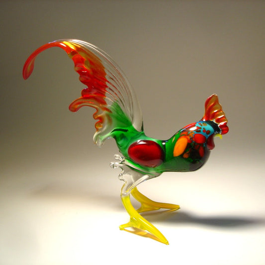 A side view of a glass rooster figurine showcasing its  red and clear tail feathers, detailed green body, and proud stance.