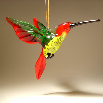 A vibrant red, green  and yellow glass hummingbird ornament with  a long pointed beak.