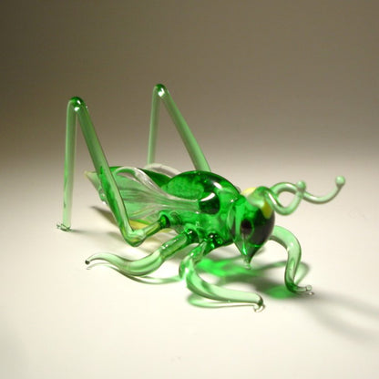 Green glass grasshopper on a beige background
