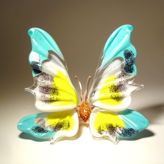 front view of the standing butterfly. It's blue with white and yellow on it's wings