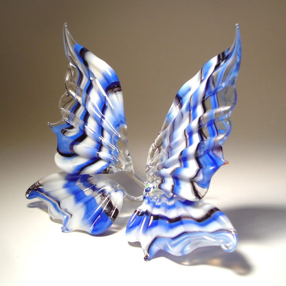 A side view of a white and blue striped glass butterfly figurine, highlighting the elegant curves of its wings and the detailed blue stripes.