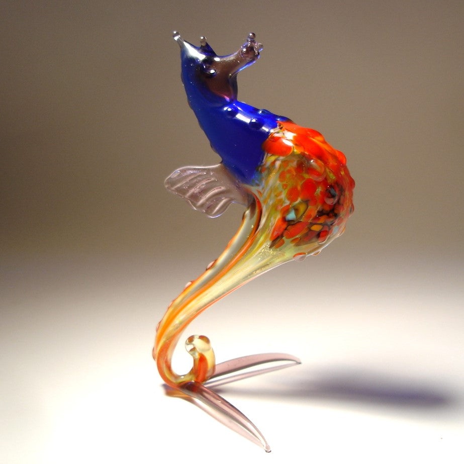 A glass figurine of a seahorse with a blue and orange body , standing upright on its tail.