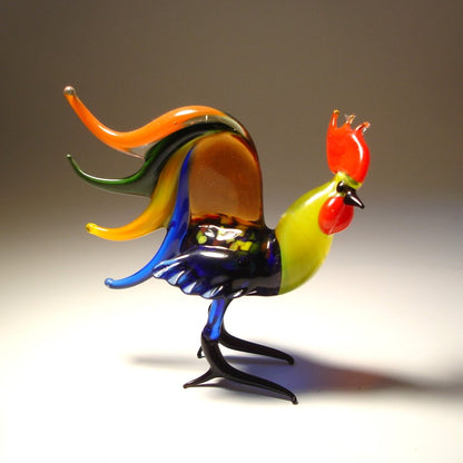 A side view of a glass rooster figurine, highlighting its impressive, colorful tail feathers that fan out elegantly.