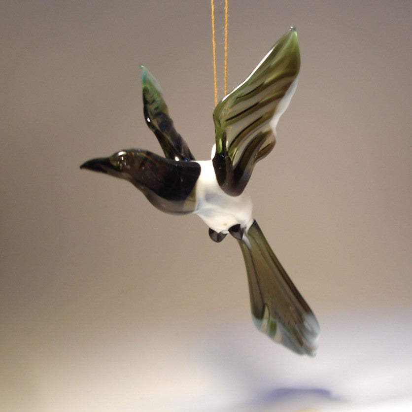 A glass Hanging Bird Magpie figurine ornament, suspended from a thread, showcasing its distinctive black and white feathers 