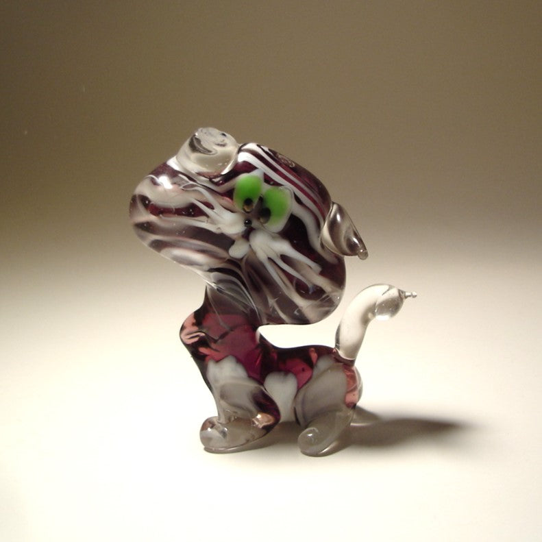 A front view of a glass striped cat figurine, showcasing its green eyes, detailed facial features, and white on purple striped pattern.